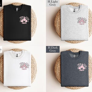 May include: Four sweatshirts in black, light gray, white, and dark gray, each featuring a pink graphic of a castle with "Disney 2024" and "mom" text. The shirts are displayed on woven mats.