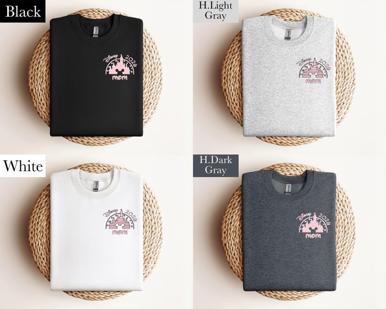 May include: Four sweatshirts in black, light gray, white, and dark gray, each featuring a pink graphic of a castle with "Disney 2024" and "mom" text. The shirts are displayed on woven mats.