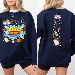K&ouml;nnte beinhalten: Marineblaues Sweatshirt mit farbenfroher Grafik. Auf der Vorderseite steht der Text "NURSE STORY" mit medizinischen Illustrationen. Die R&uuml;ckseite des Sweatshirts hat eine vertikale Anordnung &auml;hnlicher medizinischer Grafiken.