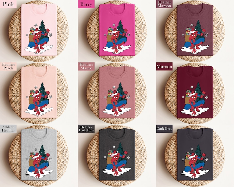 Puede incluir: Una colecci&oacute;n de camisetas en varios colores, incluyendo rosa, baya y gris, cada una con un dise&ntilde;o de superh&eacute;roe con gorro de Pap&aacute; Noel, &aacute;rbol de Navidad y regalos. Presentadas sobre esteras tejidas.