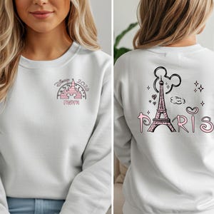 May include: White sweatshirt with a pink and black graphic on the front featuring a castle, the text "Disney 2024 Mom". The back of the sweatshirt has a pink Eiffel Tower graphic with the word "Paris".