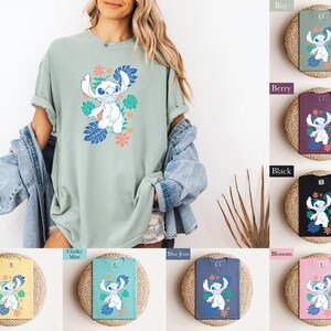 Puede incluir: Una camiseta verde claro con un personaje de dibujos animados blanco, hojas azules y flores rosas. La imagen muestra la camiseta en una persona y tambi&eacute;n muestra la camiseta en varios colores: verde, morado, negro, amarillo, azul y rosa.