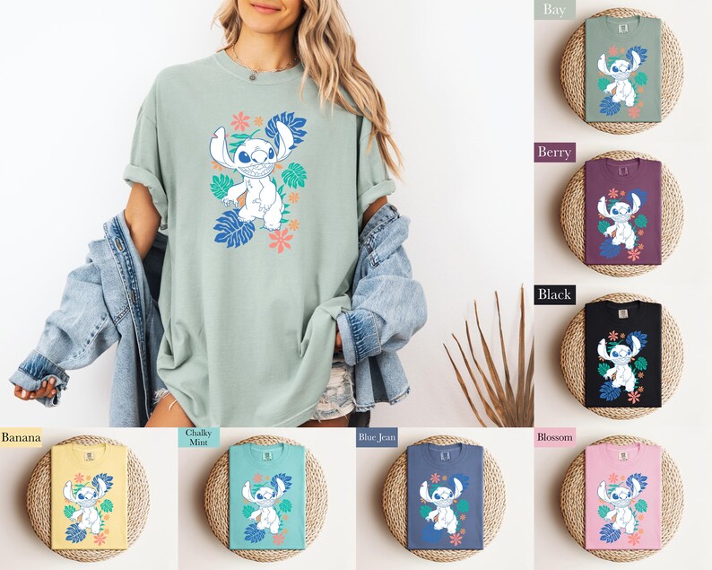 Puede incluir: Una camiseta verde claro con un personaje de dibujos animados blanco, hojas azules y flores rosas. La imagen muestra la camiseta en una persona y tambi&eacute;n muestra la camiseta en varios colores: verde, morado, negro, amarillo, azul y rosa.