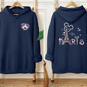May include: Navy blue hoodie with a front design featuring the text "Disney 2024 mom" and a castle graphic in pink. The back of the hoodie displays the Eiffel Tower, Mickey Mouse ears, and the word "Paris" in pink.