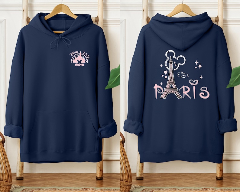 May include: Navy blue hoodie with a front design featuring the text "Disney 2024 mom" and a castle graphic in pink. The back of the hoodie displays the Eiffel Tower, Mickey Mouse ears, and the word "Paris" in pink.