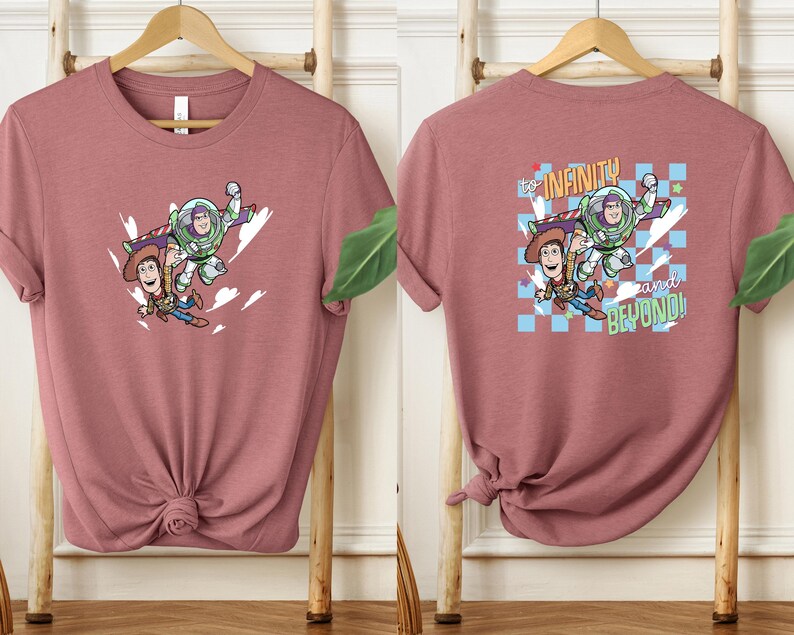Puede incluir: Camiseta rosa polvoriento con un gr&aacute;fico de Woody, Buzz Lightyear y el texto "to infinity and beyond!". La parte delantera de la camiseta muestra a los personajes en vuelo. La parte trasera de la camiseta tiene el mismo gr&aacute;fico con un fondo a cuadros.