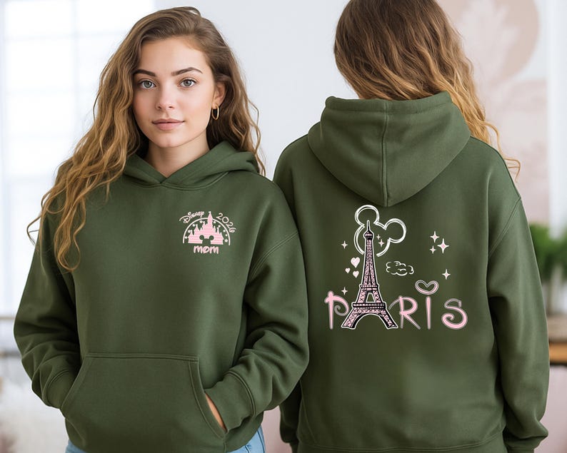 May include: Olive green hoodie with a front pocket and a hood. The front features a pink and white graphic with the text "Disney 2026 mom". The back displays a pink Eiffel Tower graphic with the word "Paris".