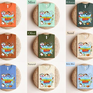 May include: A collection of t-shirts in various colors, including orange, mint, and blue. Each shirt features the text "PEDS CARE STORY" with medical-themed illustrations. The shirts are displayed on woven placemats.