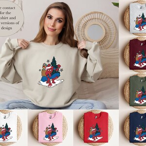 Puede incluir: Sudadera beige con un gr&aacute;fico colorido de un superh&eacute;roe con traje de Pap&aacute; Noel, llevando un &aacute;rbol de Navidad y regalos. Se muestran sudaderas adicionales en gris, burdeos, verde, blanco, rosa, rojo y azul marino. Texto en la imagen: "Please contact us for the Sweatshirt and Hoodie versions of this design."