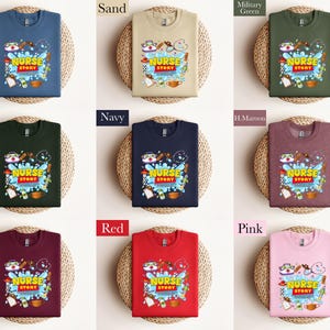 K&ouml;nnte beinhalten: Eine Auswahl an Sweatshirts in verschiedenen Farben, darunter Indigo-Blau, Sand und Rosa. Jedes Shirt zeigt eine farbenfrohe Grafik mit dem Text "NURSE STORY" und medizinischen Illustrationen.