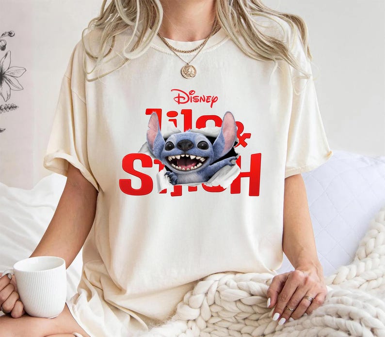 Puede incluir: Camiseta color crema con el logo de Disney y las palabras "Lilo & Stitch" en rojo. El gr&aacute;fico muestra un personaje alien&iacute;gena azul sonriendo que rompe la camiseta. Una camiseta casual y c&oacute;moda.