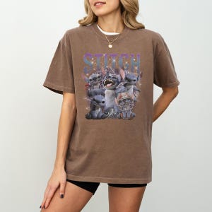 K&ouml;nnte beinhalten: Braunes T-Shirt mit einer Grafik der Figur Stitch aus dem Film Lilo & Stitch. Das Wort "Stitch" ist in einem lila-blauen Farbverlauf &uuml;ber der Figur aufgedruckt. Die Grafik zeigt Stitch mit anderen Charakteren.