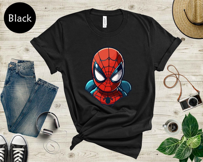 May include: Black t-shirt featuring a cartoon illustration of Spider-Man's head and shoulders. The superhero's mask is red with white eyes and blue accents. The word "Black" is in a black circle in the upper left corner.