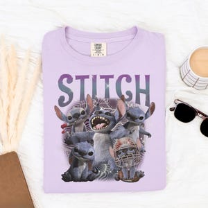 K&ouml;nnte beinhalten: Ein helllila T-Shirt mit dem Wort "STITCH" in lila aufgedruckt. Das T-Shirt zeigt eine Grafik der Figur Stitch aus dem Disney-Film Lilo & Stitch. Das Bild enth&auml;lt auch eine Sonnenbrille und eine Kaffeetasse.