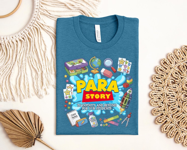 K&ouml;nnte beinhalten: T&uuml;rkisfarbenes T-Shirt mit einem farbenfrohen Grafikdesign mit den Worten "PARA STORY" in Gelb und Rot, umgeben von Illustrationen zum Thema Schule. Das Design umfasst eine Lunchbox, einen Globus, eine Rakete und den Text "TO INFINITY AND BEYOND FOR OUR STUDENTS."