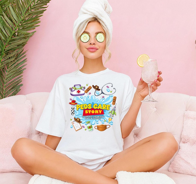 May include: White t-shirt with a colorful graphic design featuring medical-themed illustrations and the text "Peds Care Story". The design includes a stethoscope, cowboy hat, rocket, and other medical symbols. The shirt is worn by a person with a towel on their head.
