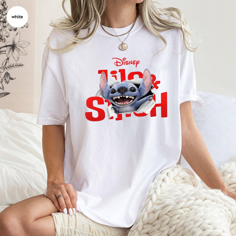 Puede incluir: Camiseta blanca con el t&iacute;tulo de la pel&iacute;cula de Disney "Lilo & Stitch" en rojo. El dise&ntilde;o muestra al personaje Stitch rompiendo la camiseta. Una prenda casual.