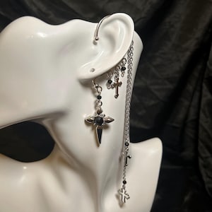 May include: Silver ear cuff with a dangling chain featuring multiple black beads and silver cross charms. The chain ends with a larger silver cross charm.