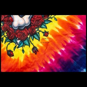Puede incluir: Una camiseta tie-dye con un patr&oacute;n de arco&iacute;ris colorido. La camiseta presenta un gr&aacute;fico de una calavera con rosas y hojas verdes. El texto "&copy; 1994 B.D.M. Inc." est&aacute; impreso en la camiseta.