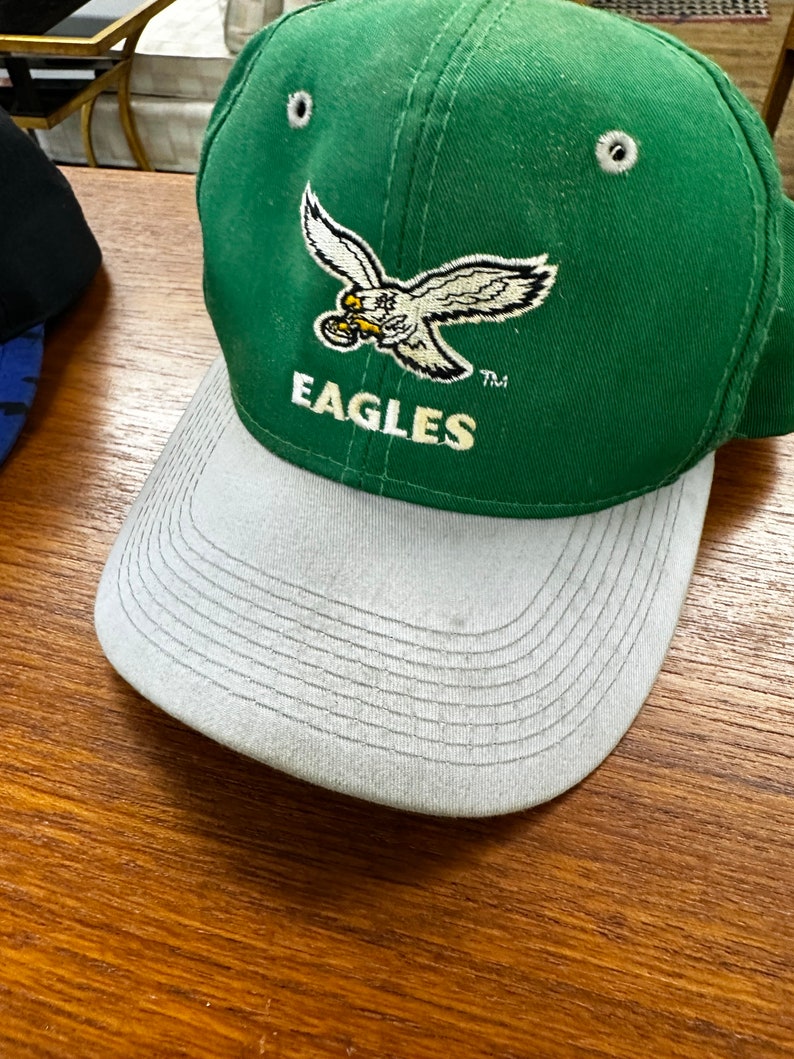 May include: Green and gray baseball cap with a white embroidered eagle and the word "EAGLES" on the front.