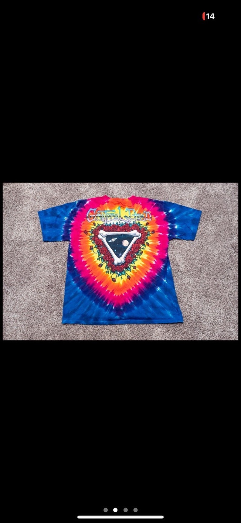 Puede incluir: Una camiseta tie-dye con un logotipo de Grateful Dead que presenta una calavera y rosas. El logotipo tiene forma de tri&aacute;ngulo con las palabras "Grateful Dead" encima.