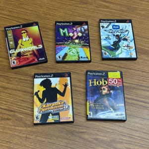 May include: A collection of ten PlayStation 2 video game cases. The cases are black with colorful artwork. The games include Clubworld, Mojo, Antigrav, Karaoke Revolution Volume 3, and The Hobbit: The Lord of the Rings.