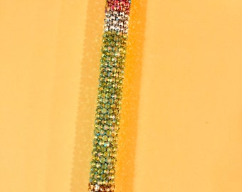 May include: A black and green pen with a silver top, covered in rhinestones. The rhinestones are arranged in a pattern of green, gold, white, and pink.