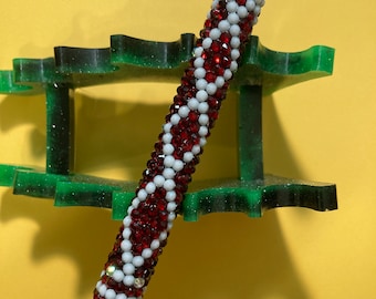 Puede incluir: Un bolígrafo rojo y blanco con joyas y una punta negra. El bolígrafo está decorado con pequeñas cuentas rojas y blancas.