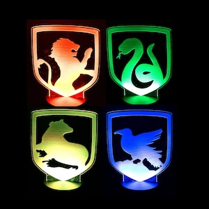 May include: Four illuminated house crests from the Harry Potter series. The crests are made of wood and feature the Hogwarts house mascots: a lion, a snake, a badger, and an eagle. Each crest is lit with a different color LED light: red, green, yellow, and blue.