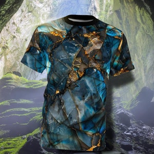 Könnte beinhalten: Ein blaues und goldenes T-Shirt mit Marmormuster. Das Shirt ist vor dem Hintergrund einer Höhle fotografiert.