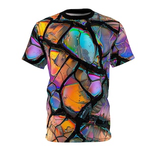Peut inclure: Un t-shirt à manches courtes avec un imprimé abstrait coloré de formes ressemblant à du verre iridescent, craquelé et brisé. L'imprimé est dans des tons de bleu, violet, orange et jaune.