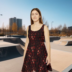 May include: A woman wearing a sleeveless black dress with a red and gold pattern stands in front of a concrete skate park.