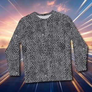 Puede incluir: Una camiseta de manga larga con un diseño de cota de malla. La camiseta es gris y negra, con cuello redondo y puños abotonados. El fondo presenta una puesta de sol y siluetas de soldados.