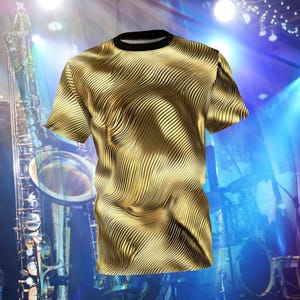 May include: A gold t-shirt with a wavy, abstract pattern. The shirt is photographed in front of a stage with lights and a saxophone.