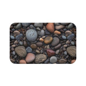 May include: A rectangular bath mat featuring a close-up of smooth, colorful river rocks. The stones vary in size and color, including shades of gray, brown, orange, and red. The mat has rounded corners and a natural, earthy aesthetic.