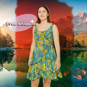 Könnte beinhalten: Ein ärmelloses Kleid mit Rundhalsausschnitt, das einen tealfarbenen Hintergrund und ein gelbes Blumenmuster aufweist. Das knielange Kleid wird von einer Person vor einer malerischen See- und Bergkulisse getragen.