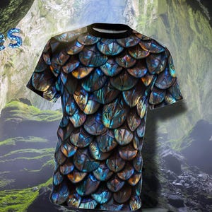 May include: A black t-shirt with a blue and green iridescent scale pattern. The shirt is photographed in front of a cave opening.