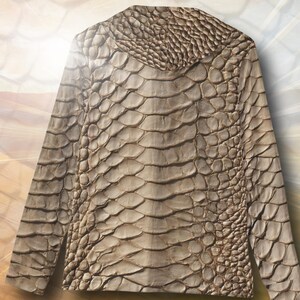 May include: A long-sleeved shirt featuring a textured, tan-colored pattern that mimics the appearance of reptile scales. The garment has a crew neckline and a consistent, repeating scale-like design across the entire front surface of the fabric.