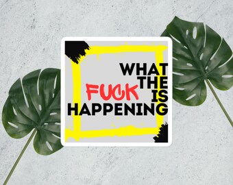 Può includere: Adesivo quadrato con la scritta "WHAT THE FUCK IS HAPPENING" in nero e rosso, incorniciata da un bordo giallo e pennellate nere. L'adesivo è su uno sfondo grigio con foglie verdi.