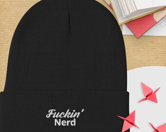 Può includere: Berretto nero con la scritta ricamata "Fuckin' Nerd" in bianco. Il berretto è realizzato in morbido materiale a maglia. Un accessorio invernale.