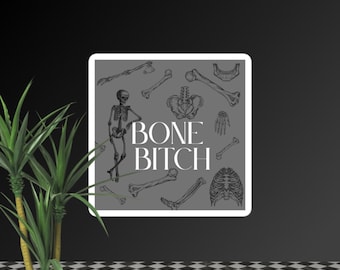 Può includere: Un adesivo quadrato con sfondo grigio raffigurante varie ossa scheletriche e la scritta "BONE BITCH" in bianco. Uno scheletro completo è raffigurato sul lato sinistro, con altre ossa sparse intorno al testo.