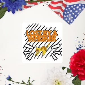 May include: Square sticker with the text "LOST BY A WHISKER" in orange and a yellow cat illustration. The cat is stretching with its mouth open. The background has black diagonal lines and white space.