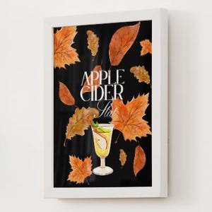 May include: A framed print featuring a watercolor illustration of an apple cider cocktail. The image has a black background with orange autumn leaves scattered around the glass. The words "Apple Cider Slush" are written in white.