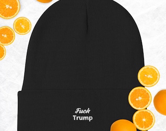 Può includere: Berretto nero con la scritta ricamata "Fuck Trump" in bianco. Il berretto è circondato da arance fresche e fette di arancia. Un accessorio invernale.