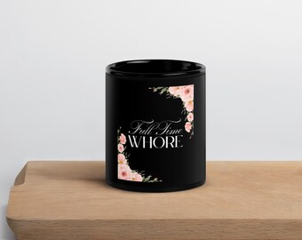 Può includere: Tazza in ceramica nera con la scritta "Full Time WHORE" in elegante corsivo, incorniciata da decorazioni floreali rosa. La tazza cilindrica è appoggiata su una superficie di legno.