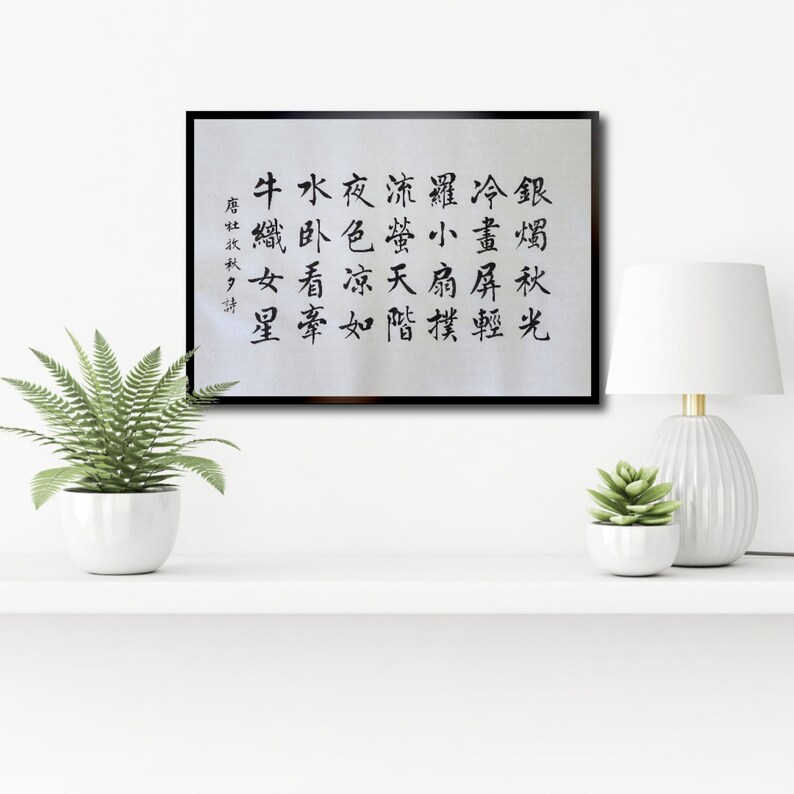 May include: Black and white calligraphy art print in a black frame with the text "牛水夜流螢冷畫屏輕羅小扇撲流螢天階夜色凉如水卧看牽牛織女星" hanging on a white wall.