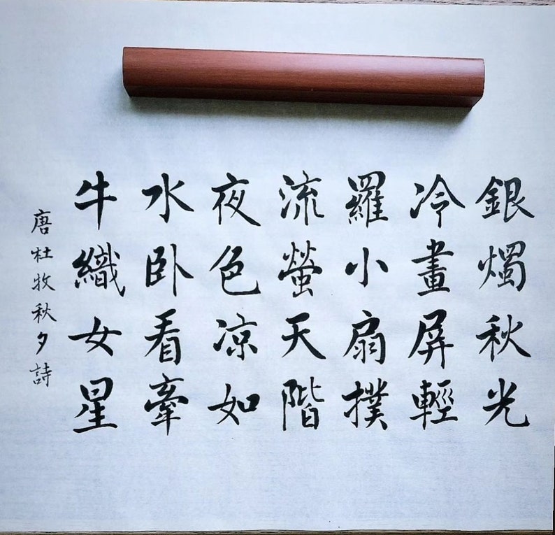 May include: Black ink calligraphy on white paper with the text "銀燭秋光冷畫屏輕羅小扇撲流螢天階夜色凉如水卧看牽牛織女星" written in traditional Chinese characters.