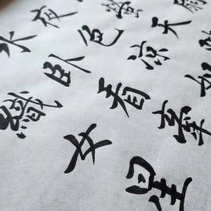May include: Close-up of black ink calligraphy on white paper. The characters are written in a traditional Japanese style.