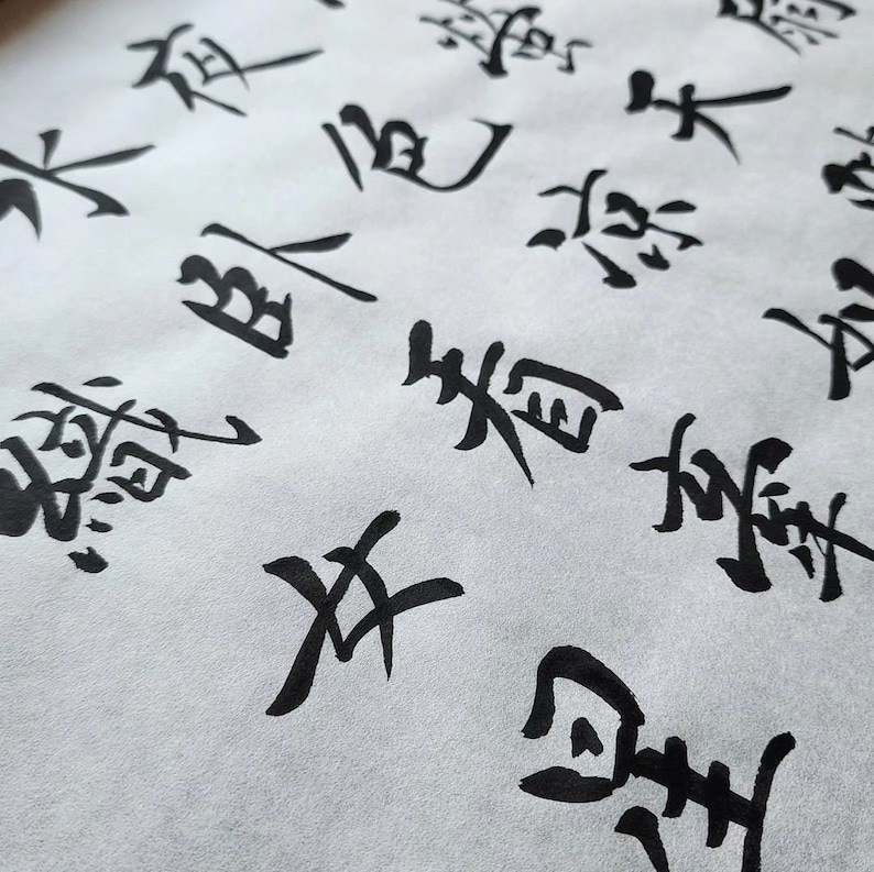 May include: Close-up of black ink calligraphy on white paper. The characters are written in a traditional Japanese style.