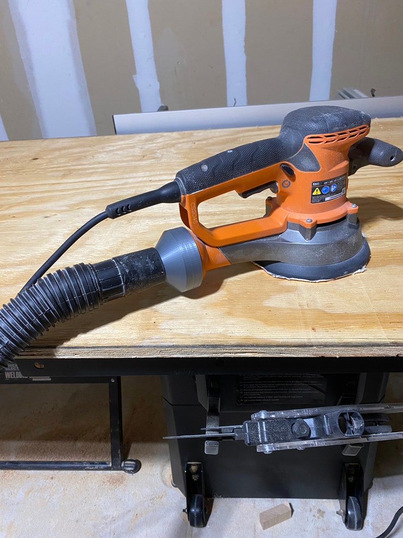 May include: An orange and black power sander with a dust collection hose attached. The sander is sitting on a wooden table.